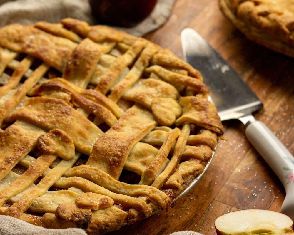 Still life: whole apple pie on a wooden board, apples and linen, side light
